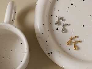 Dettaglio di orecchini a goccia in argento e oro in un vassoio di ceramica con finitura