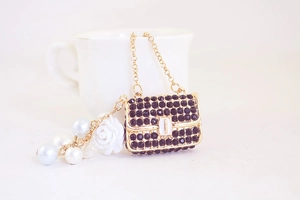 Close-up of golden handbag charm with black rhinestones and white rose pendant
