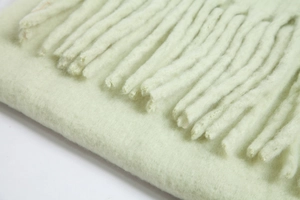 Close-up of soft green mohair scarf showing thick fringe detail and fluffy texture