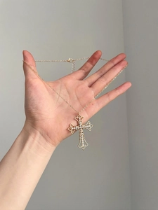 Close-up of gold cross pendant with heart pattern and sparkling crystals on hand