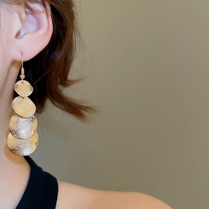 Close-up of golden cascading textured disk earrings worn by a model on a soft background