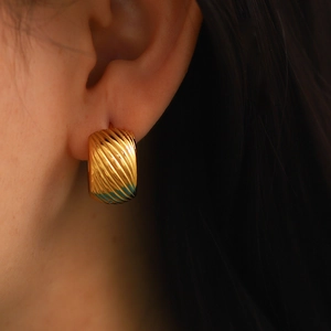 Close-up of gold wide hoop earrings with textured ripple design on female model's ear