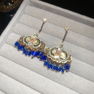 Gros plan de boucles d'oreilles dorées vintage avec cristaux et pompons en perles bleues
