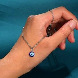 Detailed view of silver evil eye necklace held in hand against teal fabric backdrop