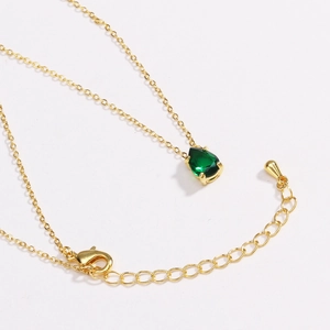 Close-up of gold chain necklace with pear-shaped emerald green pendant and lobster clasp