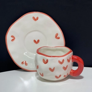 Detailed view of irregular handmade ceramic coffee cup and saucer with red heart patterns