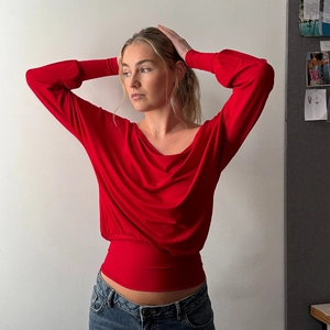 Detail of red long sleeve top with draped scoop neck and wide cinched waist design