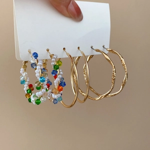 Detailed view of three pairs of gold hoop earrings with colorful beads and white pearls