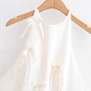 Elegant white sleeveless top with decorative satin bow hanging on a wooden hanger