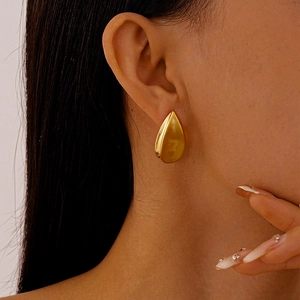 Gros plan de boucles d'oreilles gouttes dorées sur un mannequin au design fluide en métal