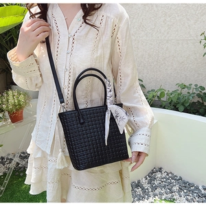 Close-up of black woven bucket bag with elegant silk scarf wrap and slim shoulder strap