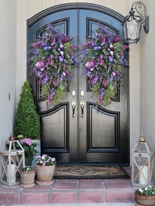 Detail of two large artificial purple tulip floral swags hanging on a black front door