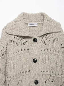 Detail view of beige hollow knit cardigan texture with black buttons and collar