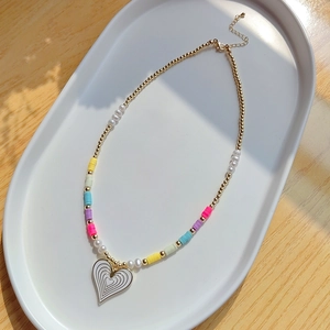 Detailed view of daisy beaded necklace with white enamel heart pendant on ceramic plate