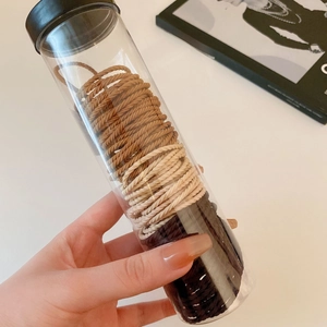 Hand holding a container of elastic spiral hair ties in neutral brown and beige tones