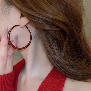 Close-up of model wearing large burgundy twisted hoop earrings with a glossy finish