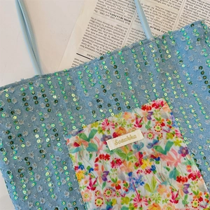 Détail du sac cabas en denim bleu clair avec sequins verts et poche à fleurs colorées