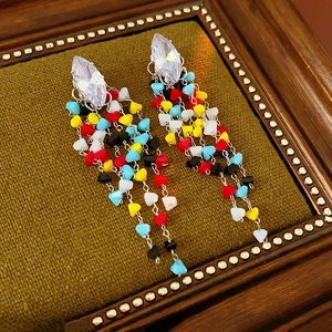 Detail of rhombic zircon earrings with colorful glass tassels on green velvet