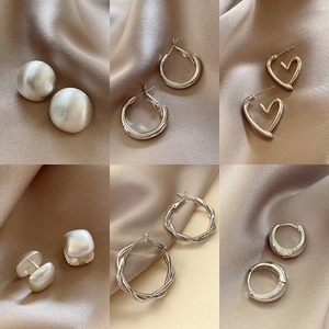 Set of six minimalist silver earrings with diverse geometric shapes on silk background