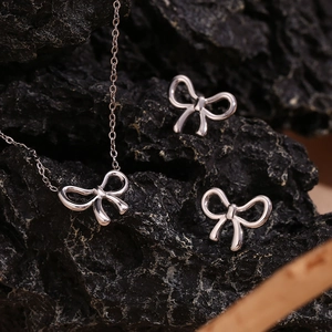 Detailed view of silver bow-shaped necklace and stud earrings set on dark stone background