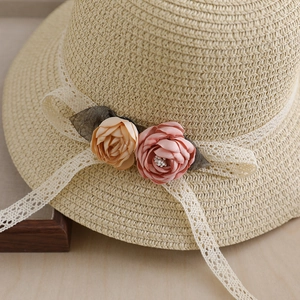 Detailed view of handmade straw hat with silk flowers and white lace ribbon trim