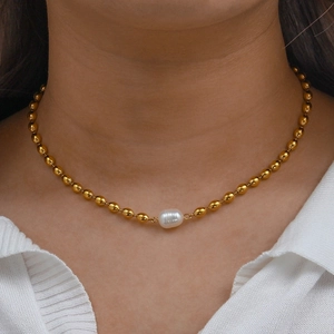 Detail of gold oval beads and a centered white pearl on a necklace worn by a model