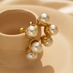 Detailed close-up of 18k gold plated curved earrings with white pearls on a ceramic dish