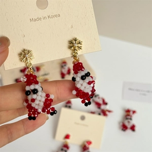 Detailed close-up of Santa Claus beaded earrings with golden snowflake stud held by fingers