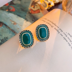 Detail of vintage oval green gemstone earrings with gold braided metal border on a book