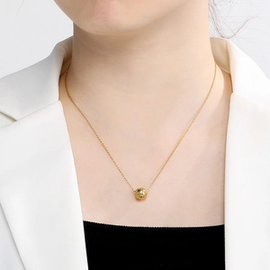 Detail shot of a minimalist gold necklace with a hollow spherical bead on a female model