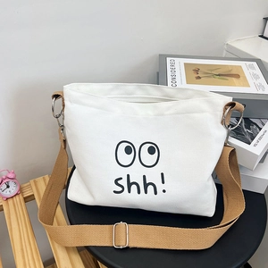Detail of white canvas bag featuring cartoon eyes and 'shh!' print with brown strap