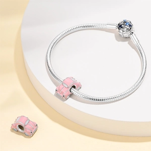 Silver snake chain bracelet with pink car charm and blue zircon bead on a white tray