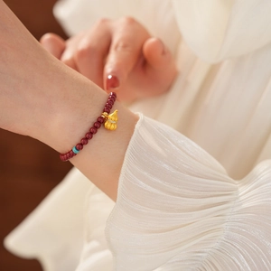 Detailed shot of cinnabar bead bracelet with gold gourd pendant on model's wrist