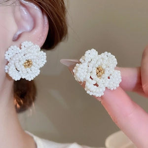 Detailed macro view of handmade camellia earrings with white beads and golden stamen