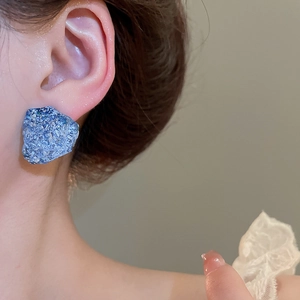 Close-up of irregular blue resin stud earrings with ice crack texture on female model