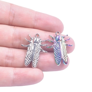 Close-up of cicada metal pendants in silver and rainbow finish held in hand