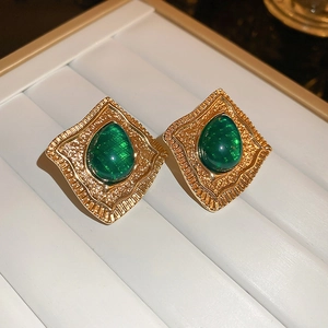 Vintage gold earrings with emerald green teardrop stones on white jewelry tray