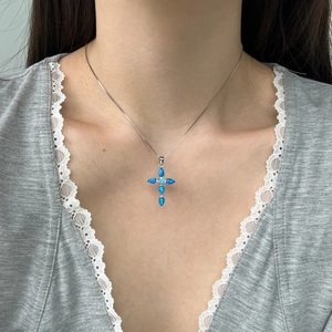 Detail of S925 silver cross necklace with blue opal stones worn on a lace garment