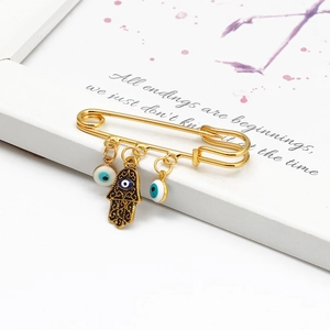 Close-up of golden Hamsa hand and blue Evil Eye charms on a metal safety brooch pin