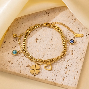 Detalle de pulsera de acero dorada de doble capa con trébol y dijes de ojo de la suerte