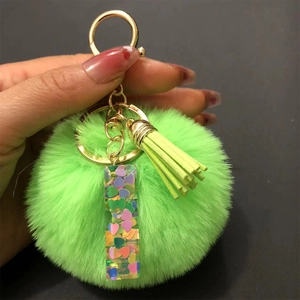 Detail of green resin keychain with heart sequins, pompom and tassel held by hand