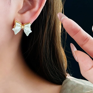 Gros plan d'un mannequin portant des boucles d'oreilles nœud blanc plaquées or 14K