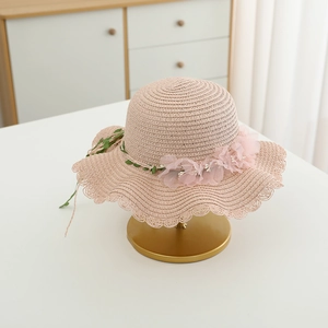 Detail of pink woven straw hat featuring delicate chiffon flowers and wavy scalloped brim