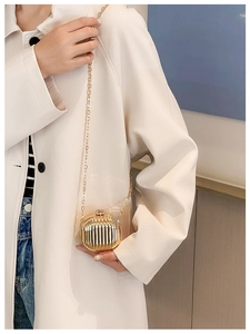 Mini gold metal suitcase-style bag with vertical grooves on model wearing cream coat