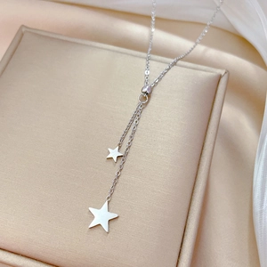 Detail of silver titanium steel necklace with double star pendants on beige cushion