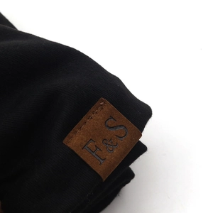 Macro view of black knitted fabric with a brown leather patch and embossed F&S logo