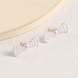 Detailed view of woven pearl bow earrings with light gold metal studs and soft luster
