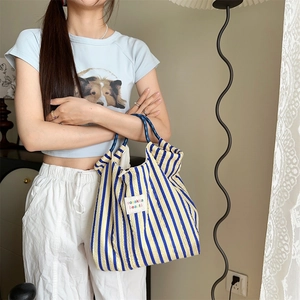 Blue and yellow striped pleated tote bag shown in a warm lifestyle indoor setting