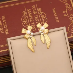 Macro shot of gold bow earrings with white pearls on a beige jewelry display stand
