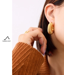Close-up of golden ribbed texture hoop earrings in stainless steel worn by a model